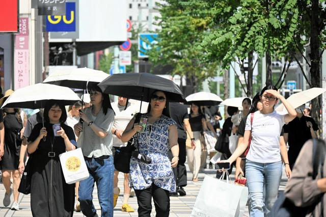 街を歩いている人たちが、日傘をさしたり、手で日をよけたりしている
