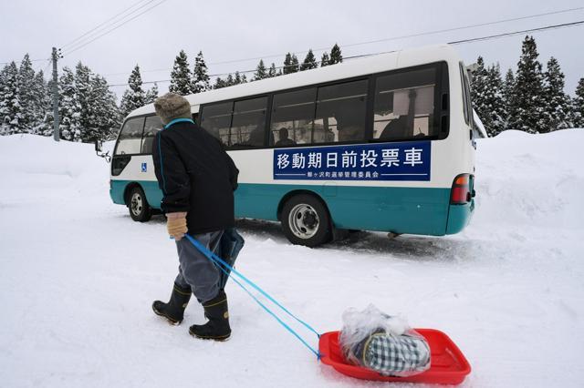 集落に駐車した移動期日前投票車。そりで荷物を運ぶ人の姿もあった