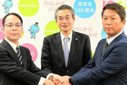 記者会見後に握手する阪神タイガースの嶌村聡・球団本部長（中央）ら。左は西宮市教委の藤岡謙一・教育長、右は元プロ野球選手の水口栄二さん