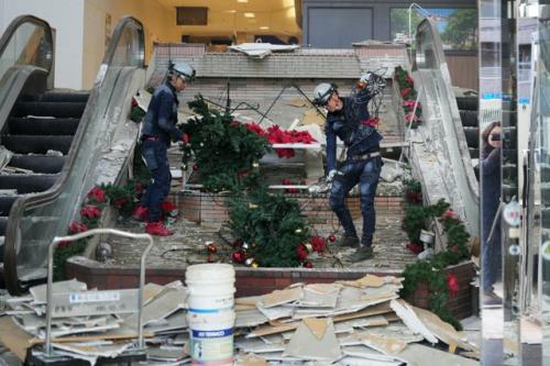 地震の影響で壁が崩落したショッピングセンターで、倒れたクリスマスツリーを撤去する作業員たち