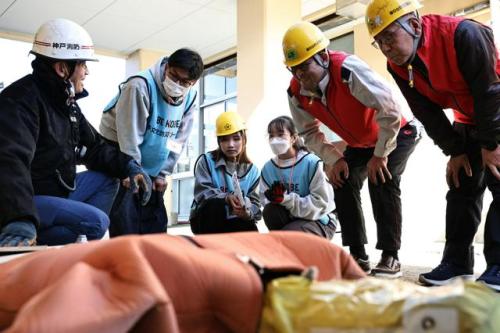 ジャッキを使った救出訓練を見守るベトナム人留学生のタオさん（左から4人目）ら