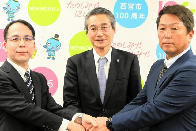 記者会見後に握手する阪神タイガースの嶌村聡・球団本部長（中央）ら。左は西宮市教委の藤岡謙一・教育長、右は元プロ野球選手の水口栄二さん